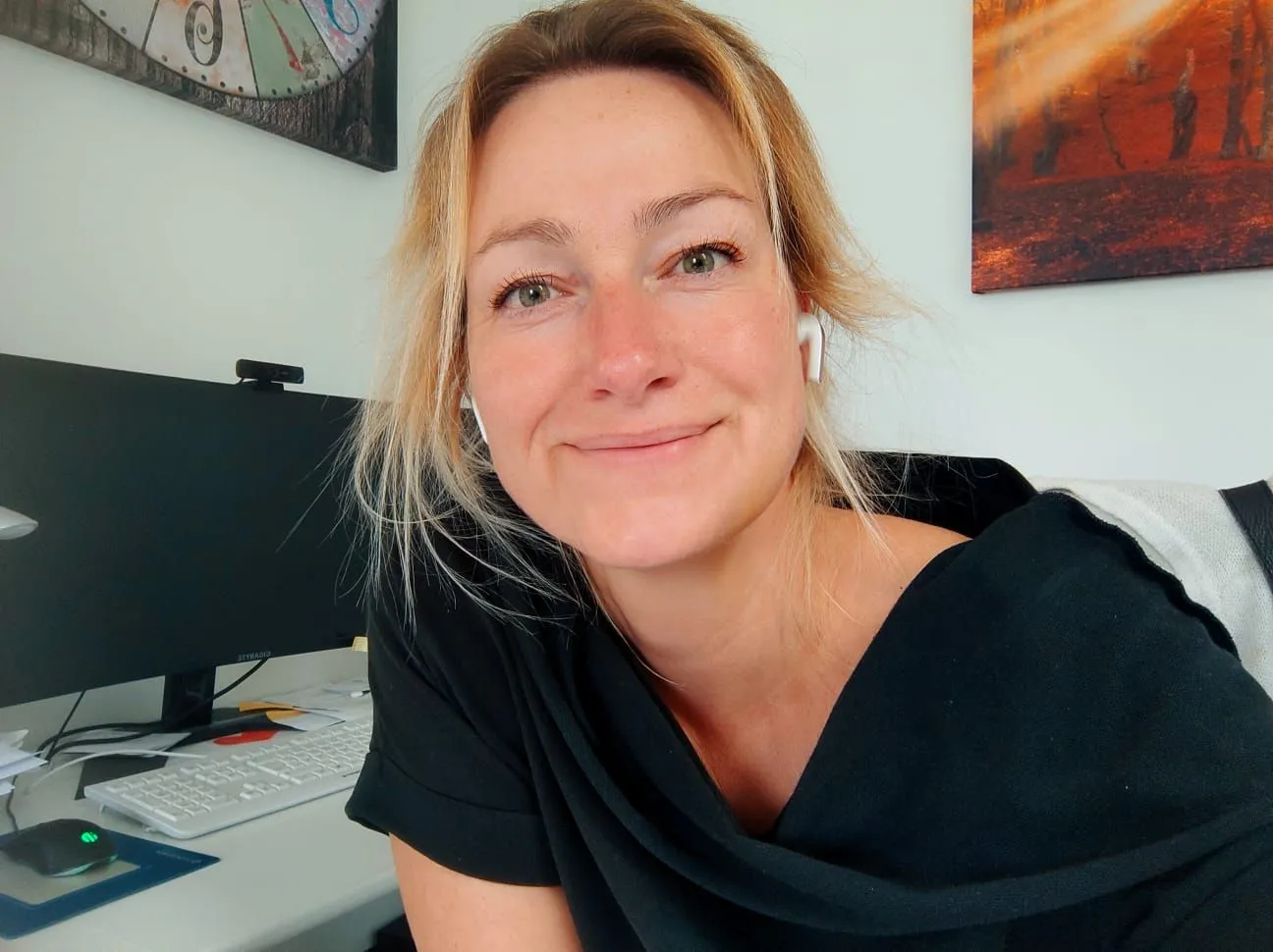 Anett blickt mit In-Ear Kopfhörern direkt in die Kamera und lächelt.