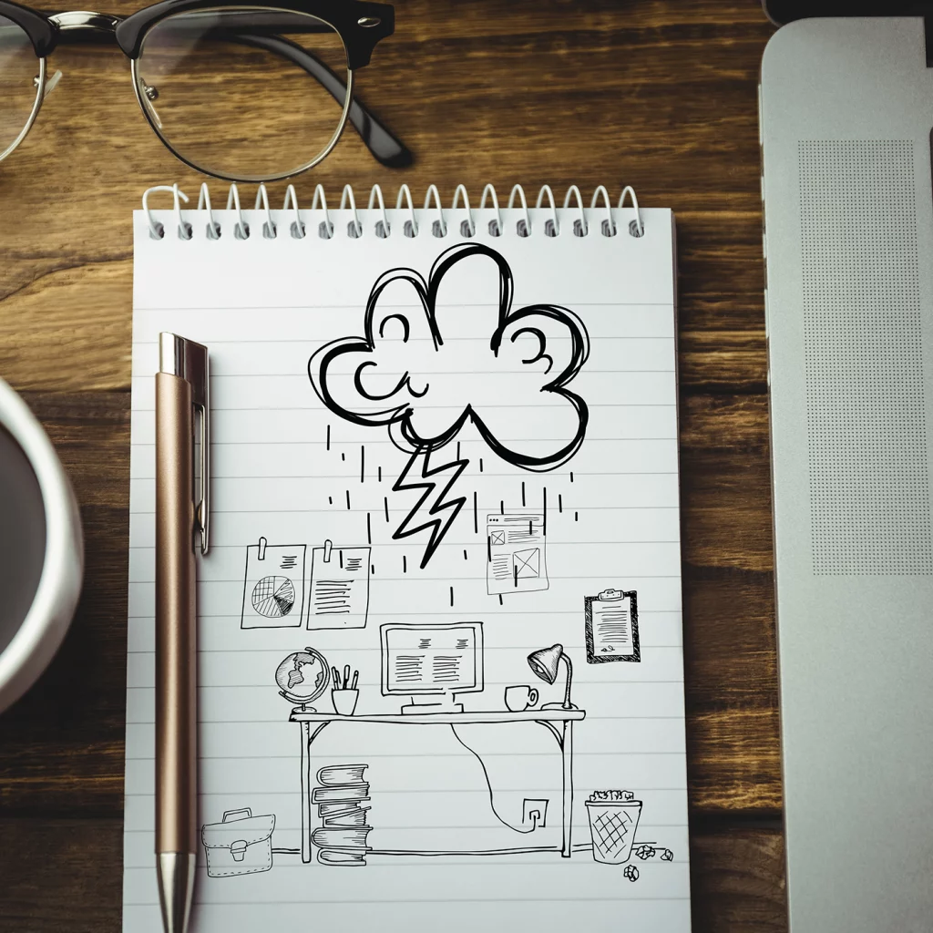 Auf einem Tisch liegen eine Brille, eine Tasse, ein Block, auf dem Scribbles gemalt sind und ein Stift