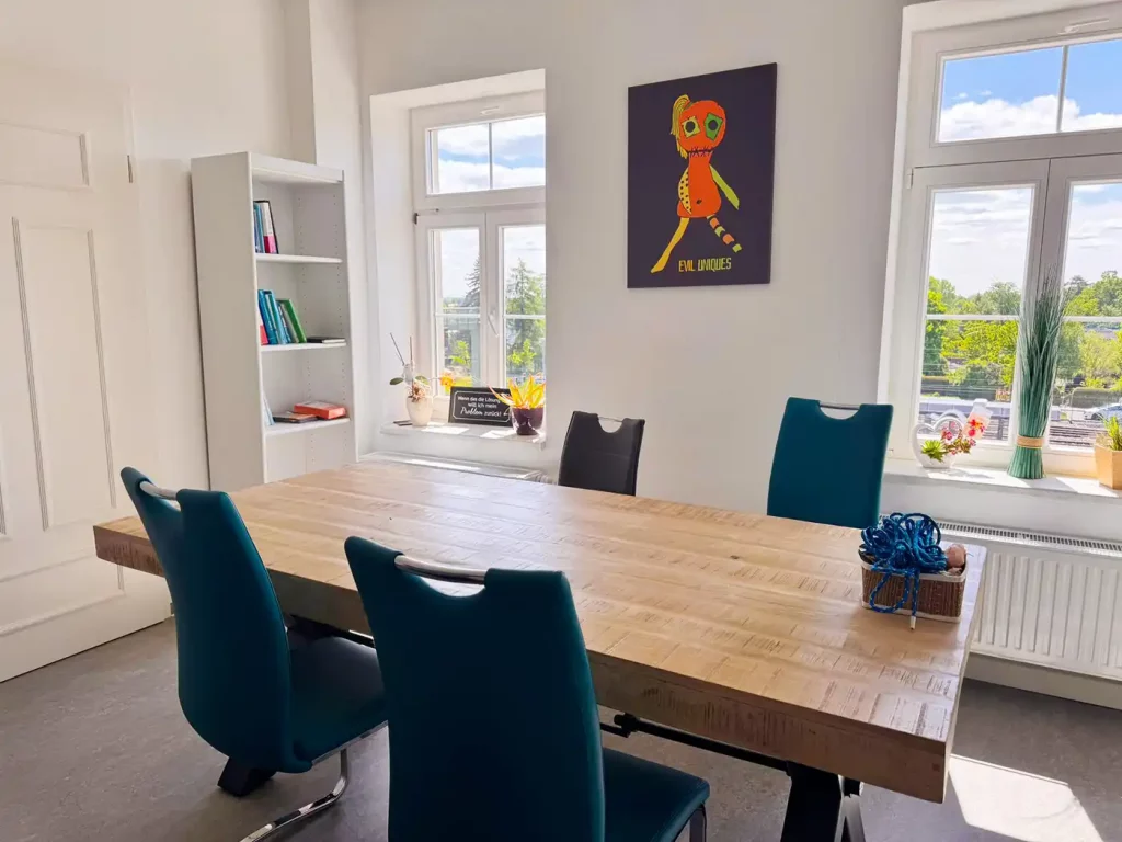 Ein Therapiezimmer mit einem Tisch, an dem 6 Stühle stehen.